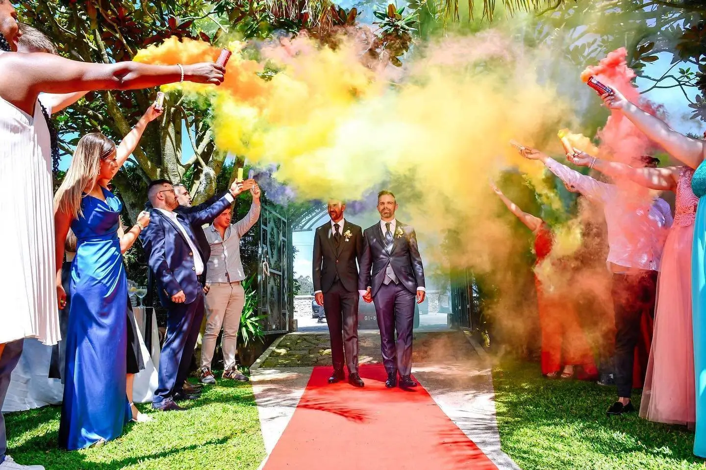 Entrada de casamento com dois noivos a caminhar pela passadeira vermelha enquanto convidados fazem disparo de fumos coloridos, parte do Pack Sunset da Joca Animação.