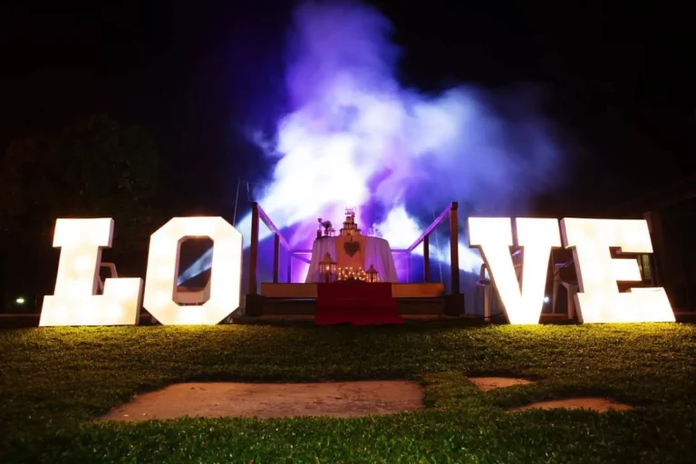 Decoração de casamento com letras luminosas LOVE e efeitos de fumo e luz, criando um cenário romântico ao ar livre.