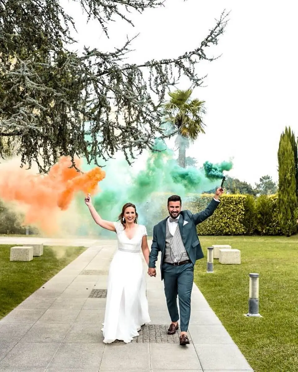 Noivos a entrar de forma festiva com fumos coloridos laranja e verde, criando um momento alegre durante o casamento.