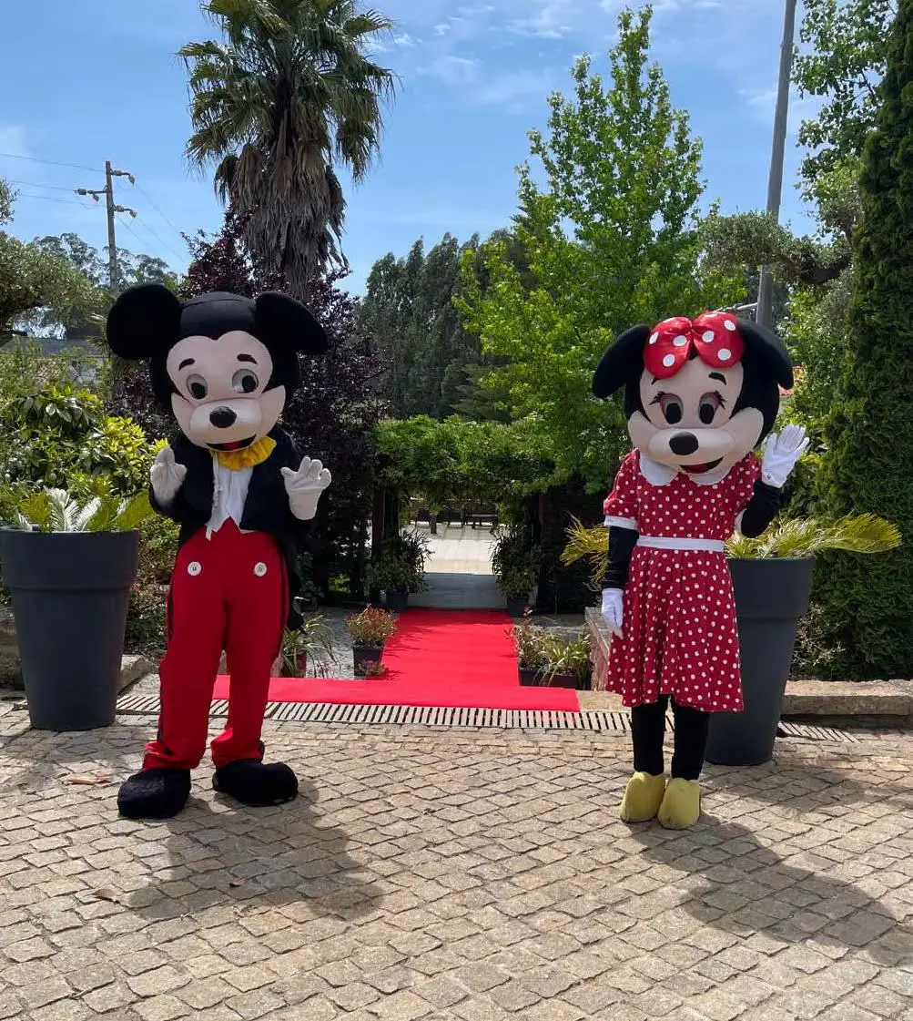 Mascotes Mickey e Minnie a receber convidados num evento infantil ao ar livre.