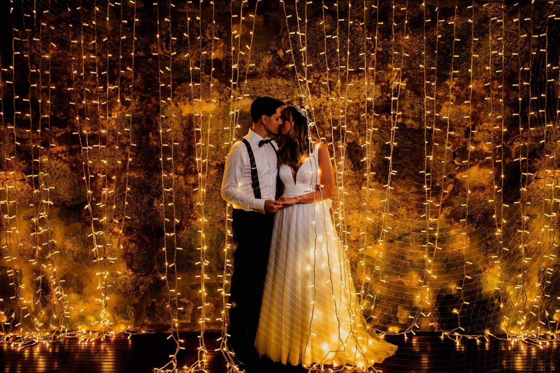 Casal de noivos junto a um cortinado de luzes quentes, simbolizando a missão da Joca Animação de criar momentos mágicos e inesquecíveis.